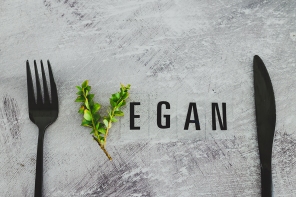 Vegan text with V made from small branches with leaves next to fork and knife, concept of healthy plant-based diet and animal rights